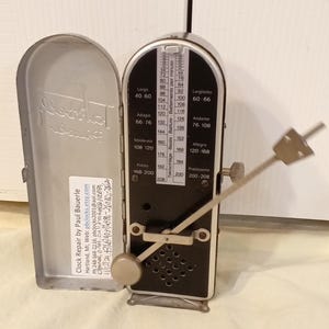 May include: A silver metronome with a black face and a silver lever. The face has markings for beats per minute from 40 to 208. The metronome is labeled "Presto" and "Prestissimo".
