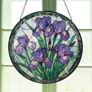 Puede incluir: Vidriera redonda con flores de iris moradas, hojas verdes y detalles amarillos. La vidriera tiene un borde de mosaico y cuelga de una cadena. El fondo es de color azul claro.