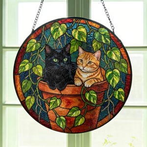 Atrapasueños de vidrieras: gatos negros y naranjas, hojas de pothos, decoración botánica para el hogar.