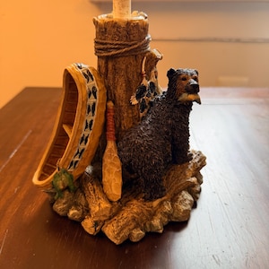 May include: A decorative lamp base featuring a sculpted black bear holding a fish in its mouth, standing next to a tree stump. The base includes a miniature canoe, a wooden paddle, and a rope detail wrapped around the textured tree trunk.