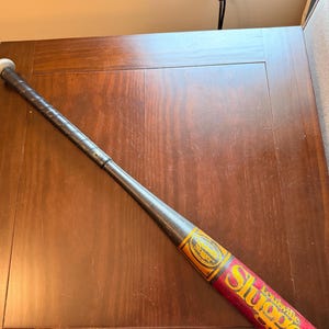 May include: A black baseball bat with a silver knob and a black grip. The barrel features a red and yellow label with the text Louisville Slugger in yellow and black lettering. The end of the barrel shows the text 21 oz printed in black.