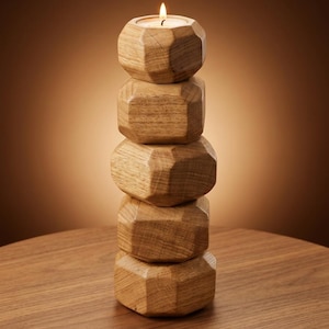 Puede incluir: Un portavelas de madera con una vela encendida. El soporte está hecho de bloques apilados de forma geométrica. El portavelas es de madera marrón claro y está sobre una mesa de madera. El fondo es un degradado de marrón.