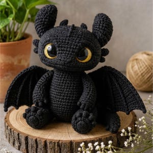 May include: A black crochet dragon plush toy featuring large, expressive yellow eyes with black pupils, pointed ears, and textured wings. The creature is crafted with detailed yarn stitching, showcasing a rounded body, small limbs, and a tail.
