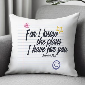 K&ouml;nnte beinhalten: Ein wei&szlig;es quadratisches Kissen mit einem linierten Notizbuch-Design, blauen horizontalen Linien und einem roten vertikalen Rand. Der Text lautet, For I know the plans I have for you, Jeremiah 29:11, mit einer rosa Blume, einem gelben Stern und einem lila Smiley.