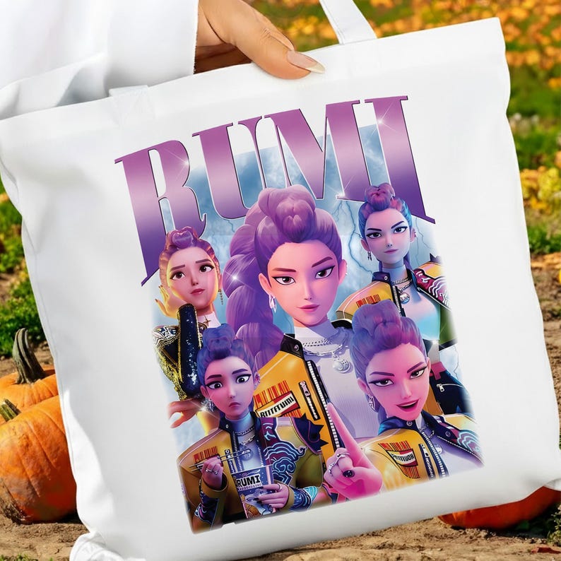 May include: White tote bag with a graphic of five stylized female figures with purple hair. The word "RUMI" is printed in large, purple letters. The figures are wearing yellow and black jackets.