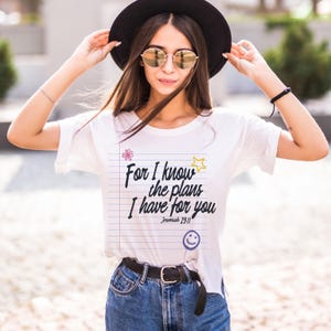 K&ouml;nnte beinhalten: Ein wei&szlig;es Kurzarm-T-Shirt mit einer Grafik aus liniertem Notizbuchpapier und dem schwarzen Text "For I know the plans I have for you Jeremiah 29:11". Das Design enth&auml;lt eine kleine rosa Blume, einen gelben Stern und ein blaues Smiley-Gesicht.