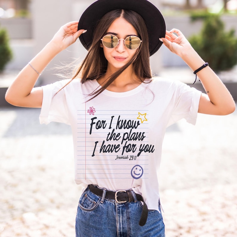 K&ouml;nnte beinhalten: Ein wei&szlig;es Kurzarm-T-Shirt mit einer Grafik aus liniertem Notizbuchpapier und dem schwarzen Text "For I know the plans I have for you Jeremiah 29:11". Das Design enth&auml;lt eine kleine rosa Blume, einen gelben Stern und ein blaues Smiley-Gesicht.