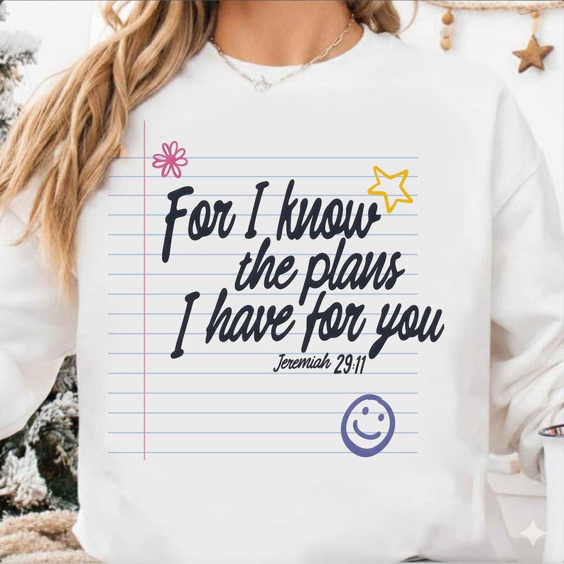 K&ouml;nnte beinhalten: Ein wei&szlig;es Langarm-Sweatshirt mit einer Grafik von liniertem Notizpapier und dem schwarzen Text "For I know the plans I have for you Jeremiah 29:11". Das Design enth&auml;lt eine rosa Blume, einen gelben Stern und ein lila Smiley-Gesicht.