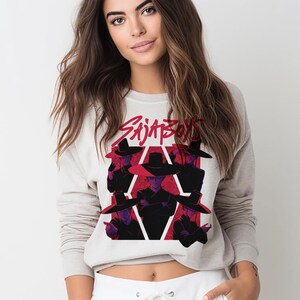 May include: A light gray sweatshirt featuring a graphic design with the text "Sajaboys" in red. The graphic includes stylized figures in black hats and coats against a red and white geometric background.