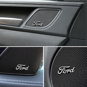 Könnte beinhalten: Nahaufnahme eines Autotür-Lautsprechergrills mit dem Ford-Logo in weißer Schrift. Der Lautsprechergrill ist schwarz und hat ein Mesh-Muster. Die Türverkleidung ist dunkelgrau.