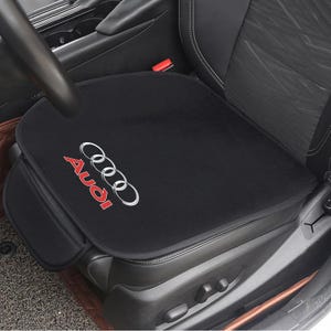 Op de afbeelding: Zwarte autostoelbekleding met het Audi-logo in rood en zilver. De bekleding is geplaatst op een zwarte autostoel. Het Audi-logo staat rechtsonder.