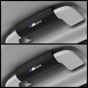 Puede incluir: Dos fundas negras para cinturón de seguridad con el logotipo de BMW en blanco, azul y rojo. Las fundas están envueltas alrededor de las manijas de liberación del cinturón de seguridad. El fondo es un interior de coche gris claro.