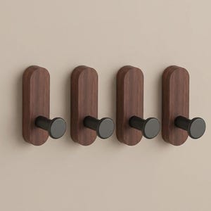 Peut inclure: Quatre patères murales disposées en rangée horizontale. Chaque patère présente une base en bois verticale de forme rectangulaire arrondie avec un grain brun foncé et une tige cylindrique noire mate avec un embout circulaire plat.