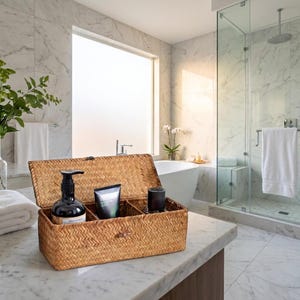 Peut inclure: Un panier de rangement rectangulaire en jonc de mer tressé avec un couvercle à charnière, doté de trois compartiments internes. Le panier contient un flacon pompe noir, un tube de soin noir et un petit récipient cylindrique noir.
