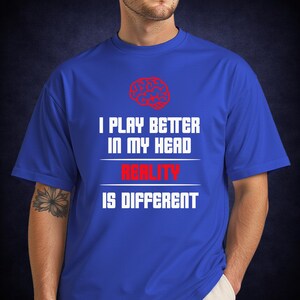 May include: Royal blue t-shirt with the text "I PLAY BETTER IN MY HEAD REALITY IS DIFFERENT" in white and red. A red brain graphic is above the text. The shirt is short-sleeved.