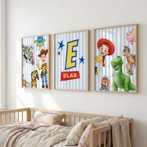 May include: Three rectangular wall art prints featuring Toy Story characters on a light blue and white striped background. The centre print displays a large yellow letter E above the red text ELAX, surrounded by blue stars.