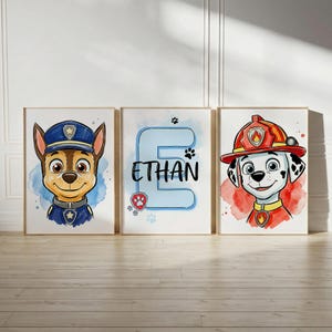 May include: Three wall art prints featuring cartoon dogs. The left print shows a brown dog in a blue police uniform. The centre print displays a large blue letter E with the name ETHAN in black text. The right print shows a white spotted dog in a red firefighter helmet.