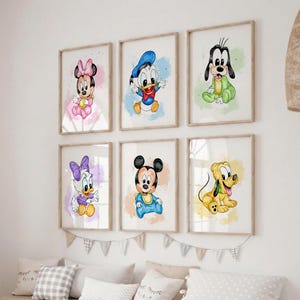 Op de afbeelding: Zes ingelijste aquarelprints met Disney-personages: Minnie Mouse, Donald Duck, Goofy, Daisy Duck, Mickey Mouse en Pluto. Elk personage is afgebeeld in een baby-achtige stijl met kleurrijke achtergronden. De prints worden boven een bed met decoratieve kussens weergegeven.