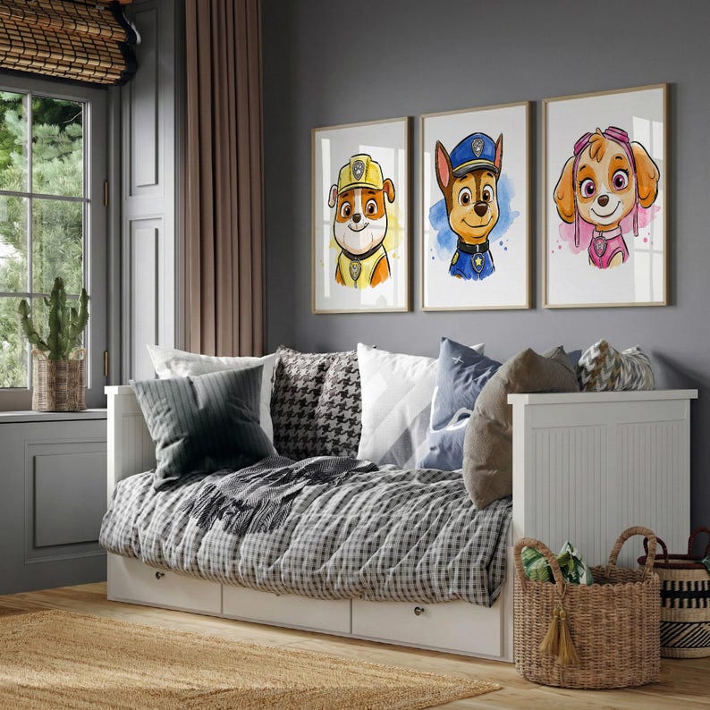 May include: Three framed watercolor prints of cartoon dogs in uniforms hang above a daybed. The prints feature a yellow, blue, and pink color scheme. The daybed has a checkered blanket, pillows, and a white frame. A woven basket sits in front.