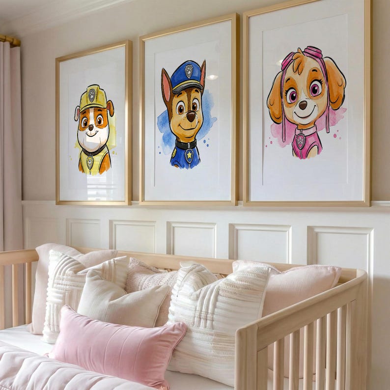 May include: Three framed watercolor prints featuring cartoon dog characters in yellow, blue, and pink outfits. The prints are displayed above a light-colored wooden crib with pink and white pillows and bedding. The frames have a gold finish.