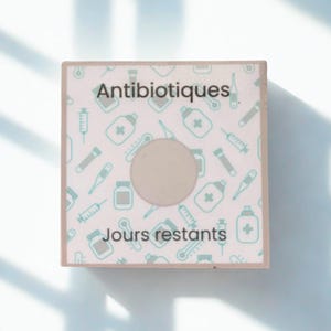 May include: A square, beige pill organizer with the words "Antibiotiques" and "Jours restants" printed on it. The organizer has a light pink background with a pattern of medical icons in teal.