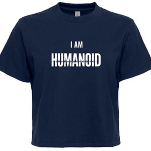 May include: Navy blue t-shirt with the white text "I AM HUMANOD". The text is centered on the front of the shirt. The shirt has short sleeves and a crew neck.