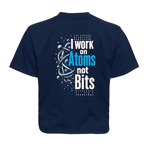May include: Navy blue t-shirt with the text "I work on Atoms not Bits" in white and blue. The design includes a graphic of an atom and binary code. A science-themed tee.
