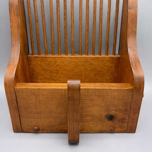 May include: A wooden dish rack with a warm, medium-brown finish. The rack features a slatted back and a lower compartment for plates. A handle is attached to the front. The design is simple and functional, suitable for kitchen organization.