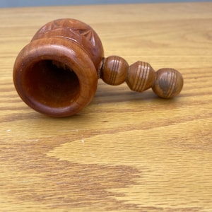May include: A wooden nutcracker with a carved floral design on the top and a series of wooden spheres attached to the side. The nutcracker is made of light brown wood and sits on a wooden surface.