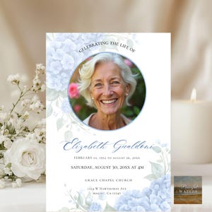 Może przedstawiać: Karta pamiątkowa ze zdjęciem uśmiechniętej starszej kobiety, otoczona ilustracjami niebieskich hortensji. Tekst brzmi "Celebrating the Life of Elizabeth Gualdeni" z datami i szczegółami usługi. Świeca i kompozycja kwiatowa są w tle.