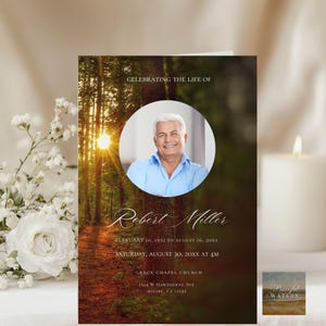 May include: A memorial card featuring a forest scene with a bright sun and a photo of a smiling man. The card reads "Celebrating the Life of Robert Miller" with dates and service details. White flowers and a lit candle are in the background.