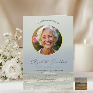 May include: A memorial card featuring a photograph of a smiling woman in a gold frame. The text reads "Celebrating the Life of Elizabeth Gualdoni" with dates and service details. The card has a watercolour ocean scene at the bottom.