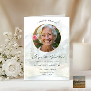 May include: A memorial card with a photo of a smiling woman in a gold-rimmed circle, with the text "Celebrating the Life of Elizabeth Gualdoni." The card includes dates, time, and the Grace Chapel Church address. The background features a watercolor mountain and forest scene.