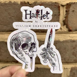 May include: A holographic sticker featuring the text Hamlet by William Shakespeare. The design includes a black and white line art illustration of a hand holding a human skull and another hand holding a dagger with a red blood-like stain on the blade.
