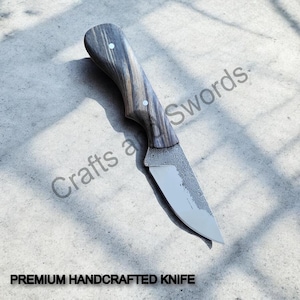 Könnte beinhalten: Ein handgefertigtes Messer mit Holzgriff und silberner Klinge. Der Griff ist eine Mischung aus Grau- und Brauntönen mit zwei kleinen weißen Akzenten. Die Klinge hat ein strukturiertes Aussehen. Der Text "PREMIUM HANDCRAFTED KNIFE" steht unten.