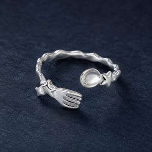 Könnte beinhalten: Ein silberfarbener offener Ring mit einem gabel- und einem löffelförmigen Ende sowie einem gewellten Ringband. Das Gabelende ist mit einem kleinen Stern verziert, und auch das Löffelende ist mit einem Stern versehen, was ein Besteckmotiv ergibt.