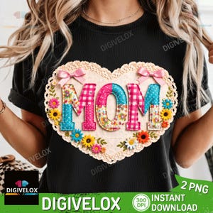 Op de afbeelding: Zwart T-shirt met een hartvormig ontwerp met het woord "MOM". De letters zijn in roze ruitjes, bloemen en blauwe stippenpatronen. Het hart is afgezet met kant en versierd met bloemen en roze strikken.