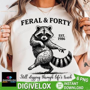 May include: A cream-colored t-shirt featuring a black graphic of a raccoon. The text reads FERAL & FORTY, EST. 1986, and Still digging through life's trash. The design is centered on the chest of the garment, showcasing a detailed illustration.