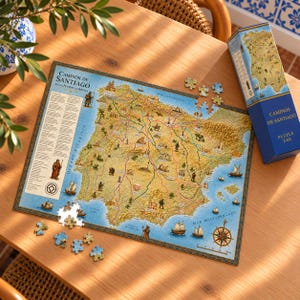 May include: A 540-piece jigsaw puzzle titled Caminos de Santiago featuring a detailed map of the Iberian Peninsula with pilgrimage routes, historical illustrations, a compass rose, and a blue box with matching map graphics.