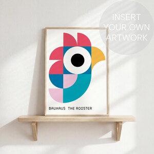 May include: A framed print featuring a geometric rooster design in red, pink, blue, yellow, and teal. The artwork, labeled "BAUHAUS THE ROOSTER," is displayed on a light wooden shelf against a white wall. The design is modern and colorful.