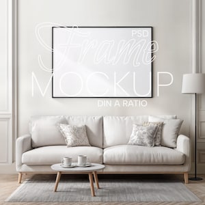 Puede incluir: Escena de salón con sofá blanco, cojines decorativos y mesa de centro redonda. Una maqueta de arte enmarcada en negro cuelga sobre el sofá. El texto "Frame Mockup DIN A Ratio" es visible. Una lámpara de pie está a la derecha.