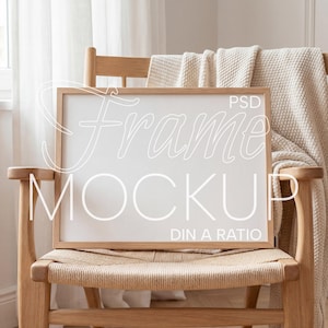 May include: A rectangular wooden frame mockup with the text "Frame Mockup" and "PSD DIN A RATIO" in white, resting on a woven chair. A beige blanket is draped over the chair's back. The scene is bathed in natural light.