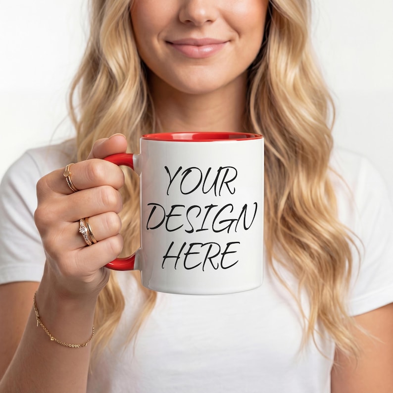 K&ouml;nnte beinhalten: Wei&szlig;e Keramik-Tasse mit rotem Innenraum und Henkel. Die Tasse tr&auml;gt den Text "YOUR DESIGN HERE" in schwarzer Schrift. Die Tasse wird von einer Person gehalten, die ein wei&szlig;es T-Shirt tr&auml;gt.