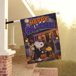 Könnte beinhalten: Eine rechteckige Gartenflagge mit Snoopy als Vampir und Woodstock als Hexe, die beide Kürbiseimer halten. Der Text HAPPY HALLOWEEN steht in großen orangefarbenen und violetten Buchstaben über einem Haus, das mit Lichtern geschmückt ist.
