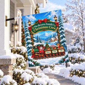 May include: A rectangular garden flag featuring a festive winter scene with a red and green steam train carrying a snowman and a reindeer. The text reads The Brown Family's Christmas Crew, with the names Thomas, Rosie, and Sam on the train cars.