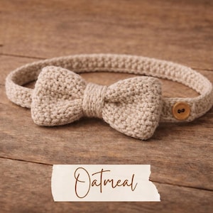 May include: A crocheted bow tie headband in oatmeal color. The bow tie is centered on the headband, with a wooden button closure on one end. The word "Oatmeal" is written in cursive on a white label.