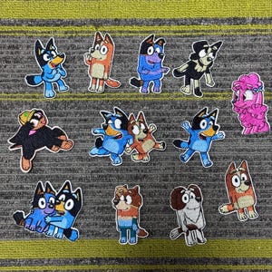 Può includere: Una collezione di toppe ricamate con personaggi di cani dei cartoni animati in varie pose e colori. Le toppe presentano cani blu, arancioni, neri e rosa, con contorni bianchi. Le toppe sono su uno sfondo a righe grigie e verdi.