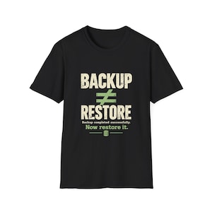May include: A black short-sleeved t-shirt featuring a graphic with the text BACKUP ≠ RESTORE in a distressed white font. Below this, the text reads Backup completed successfully. Now restore it. in white and green with a small database icon.