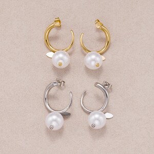 May include: Two pairs of hoop earrings, one gold-toned and one silver-toned. Each hoop features a smooth, circular design with a single white spherical pearl attached at the base, accompanied by a small, flat, leaf-shaped metal accent piece.