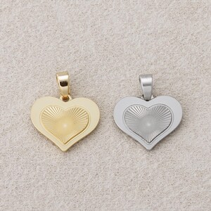 May include: Two heart-shaped pendants. One is gold-colored, the other is silver-colored. Each pendant has a raised heart design in the center with a sunburst pattern. The pendants are likely for necklaces or bracelets.